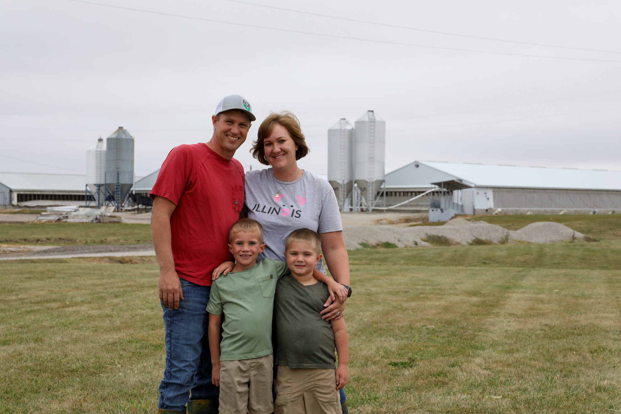 An Illinois farm family stands in front of their pig barns