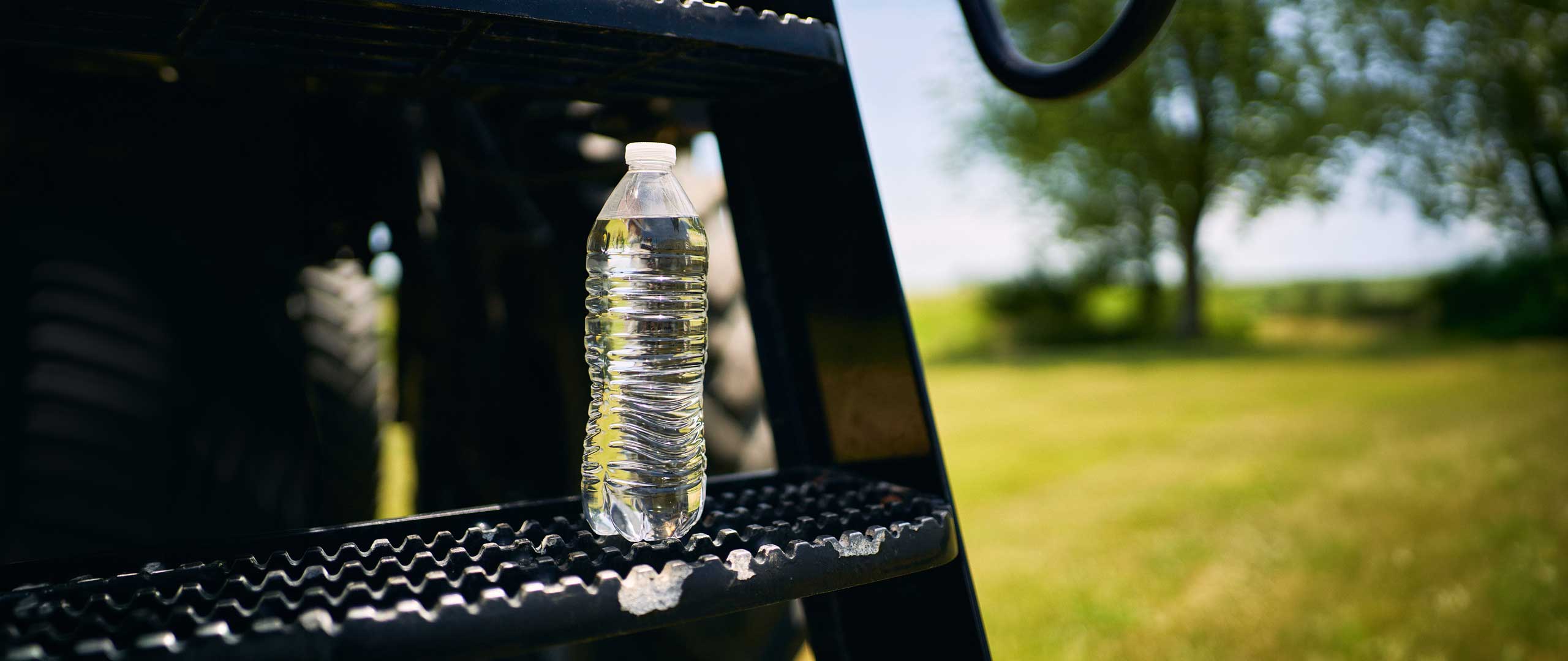 Photo of a water bottle with a farm in the background