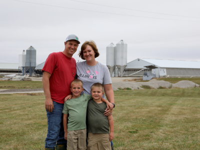 An Illinois farm family stands in front of their pig barns